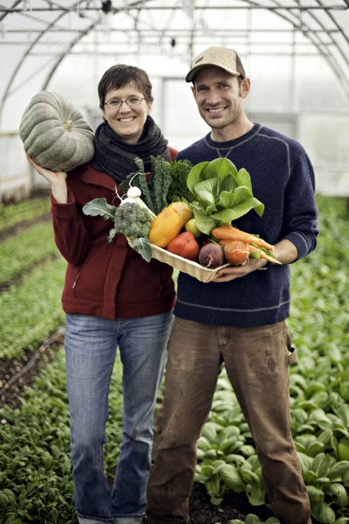 Man and a woman standing in a garden holding vegetables