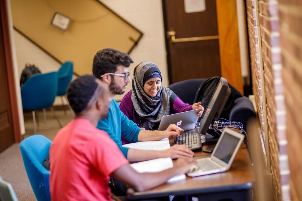 Three students working together around laptop computers