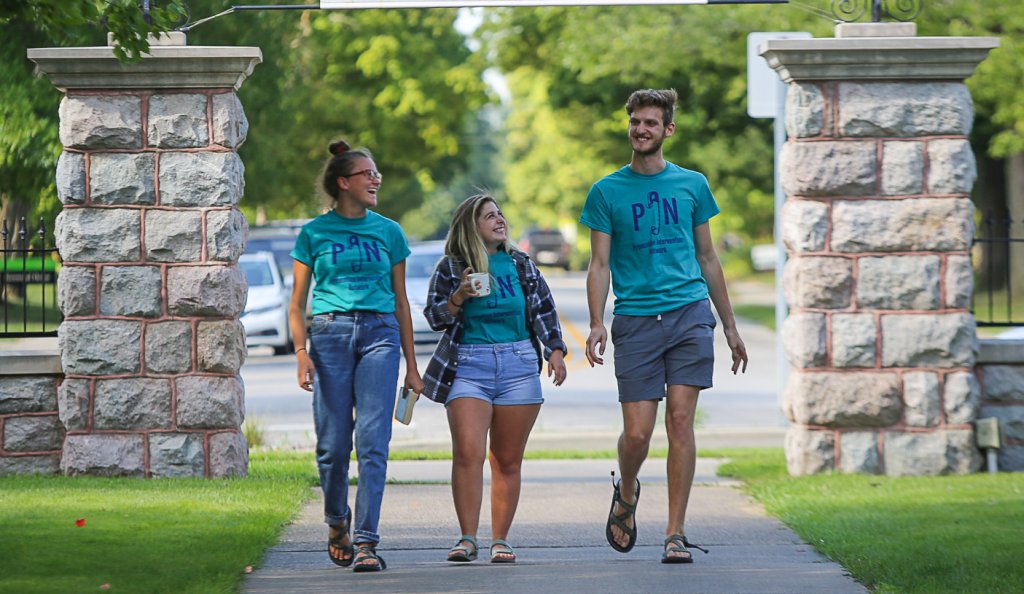 Three people wearing PIN shirts in front of Goshen College entrance