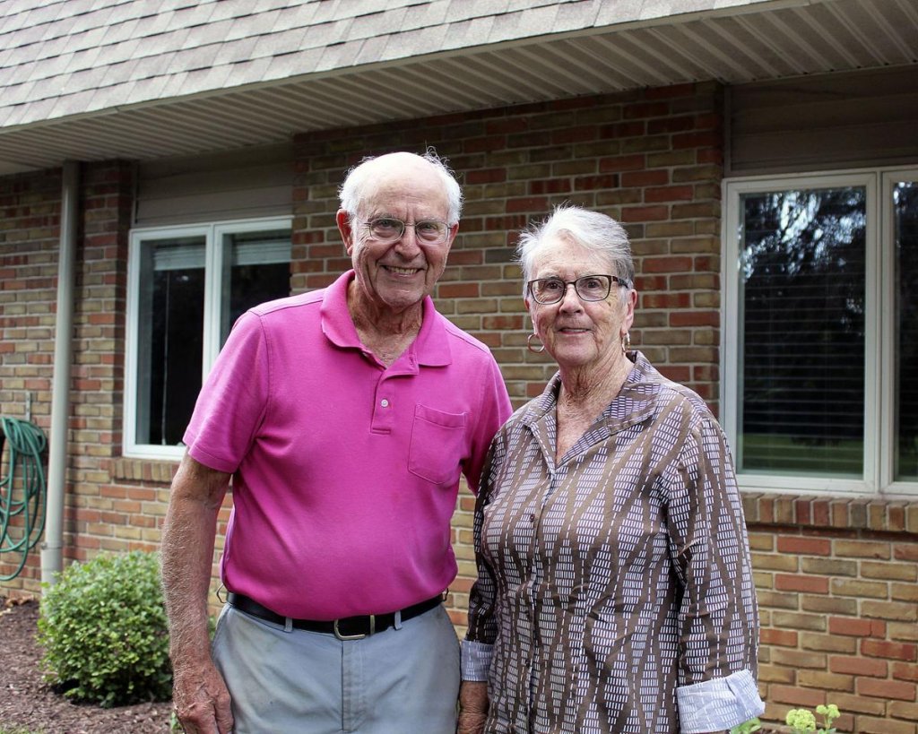 Man and a woman posing together in front of a brick house