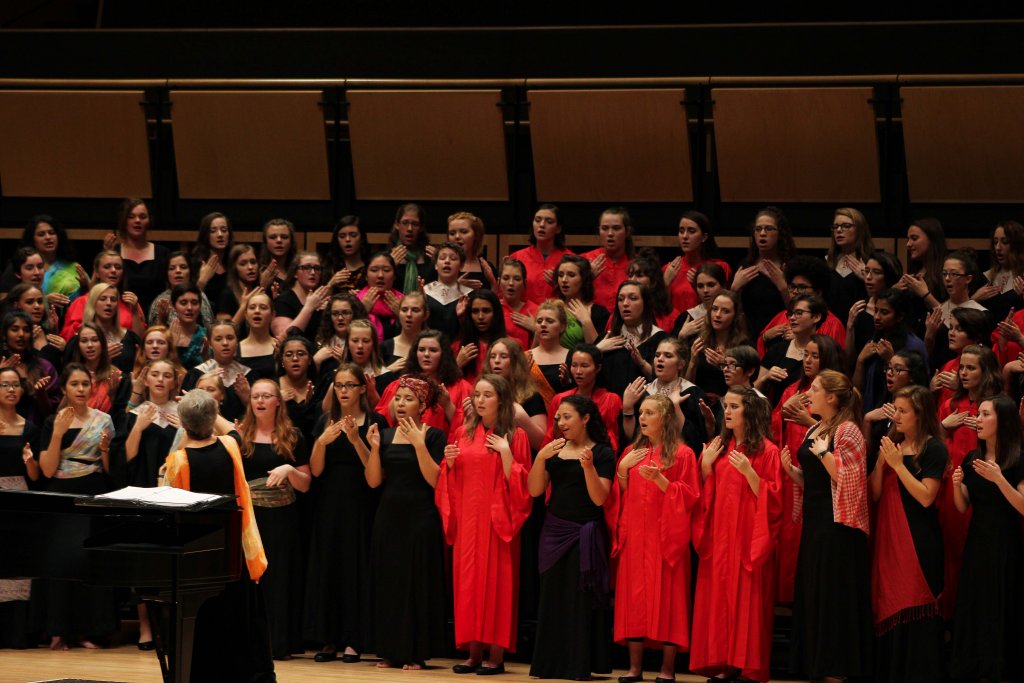 Women's choir singing. Some wearing black dresses and others wearing red