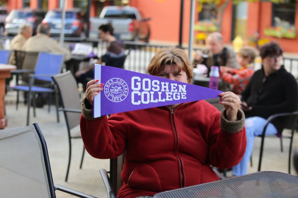 Woman holding Goshen College flag with sitting at an outside table