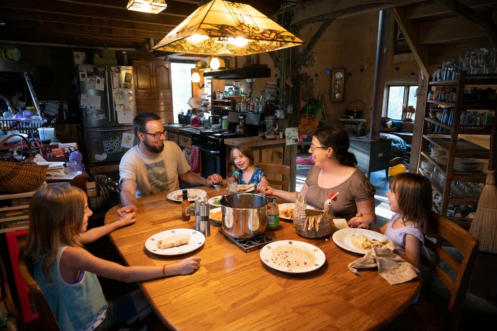 A man, woman, and three children holding hands at a table with food on the table