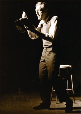 Sepia photo of a man standing and reading with a stool behind him