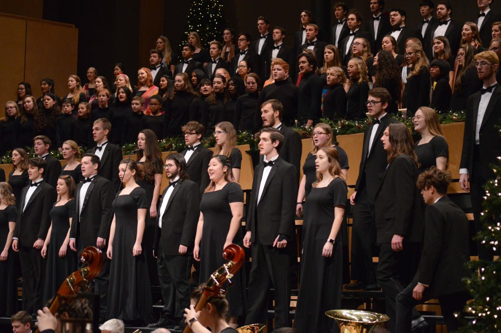 A large group of singers on stage holding music folders