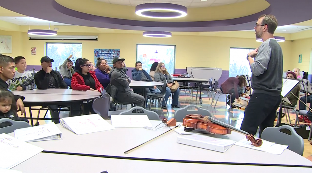 A man teaching a classroom full of students with a violin next to him