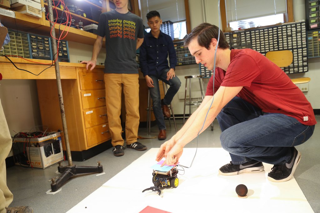 Three students, with one student working on a small wheeled robot