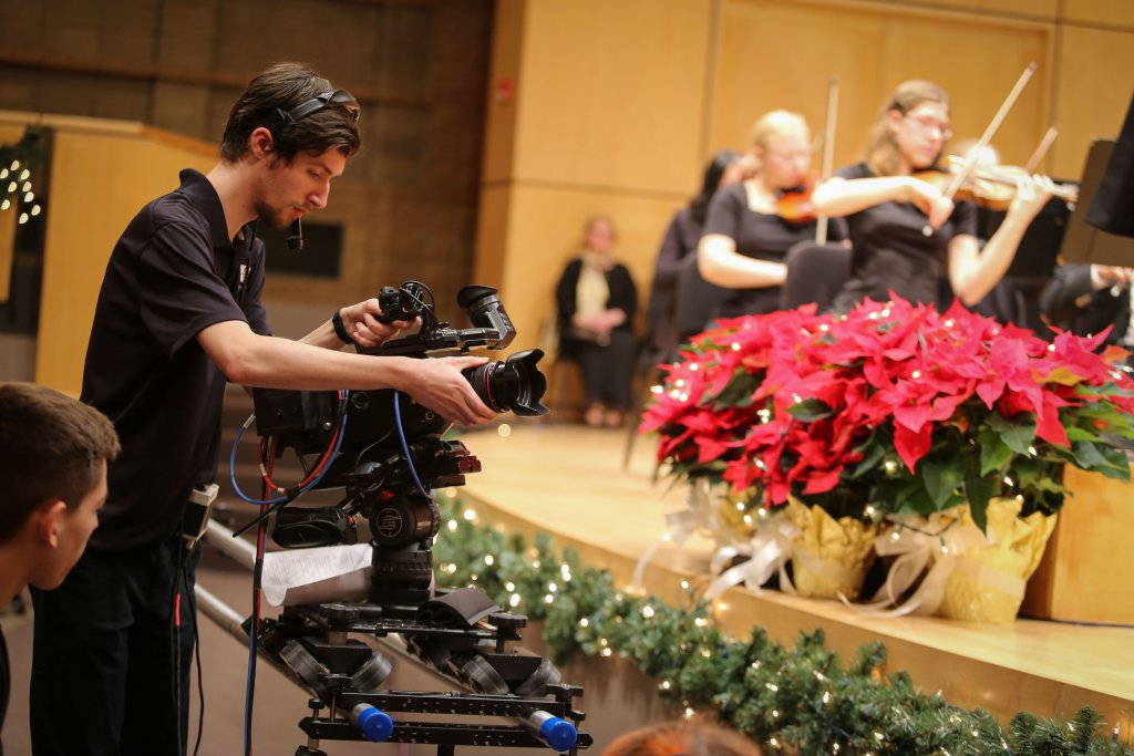 Student with a film camera in front of a concert stage.