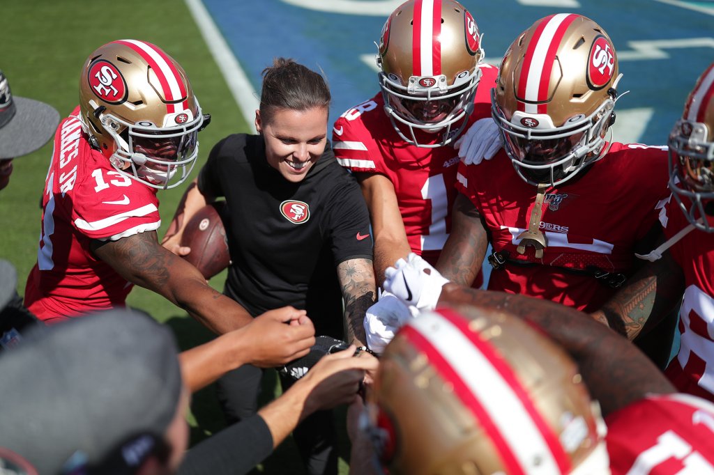 Woman standing in a huddle with a group of football players on a field