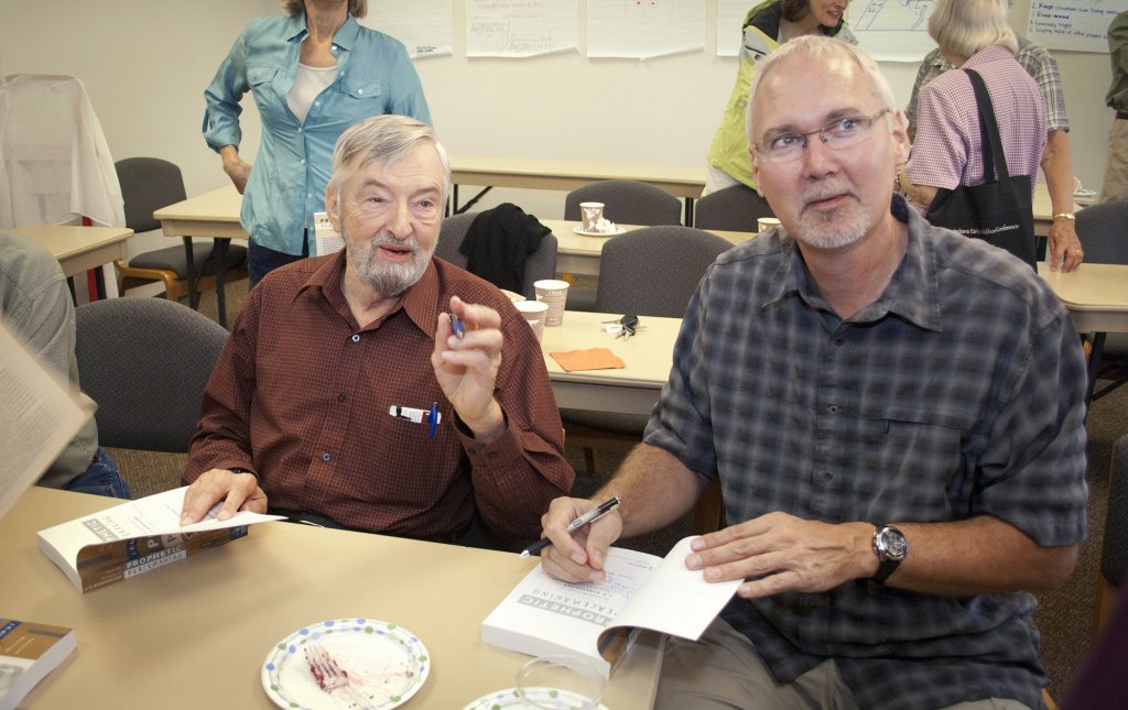 Two men sitting together at a table and looking at books