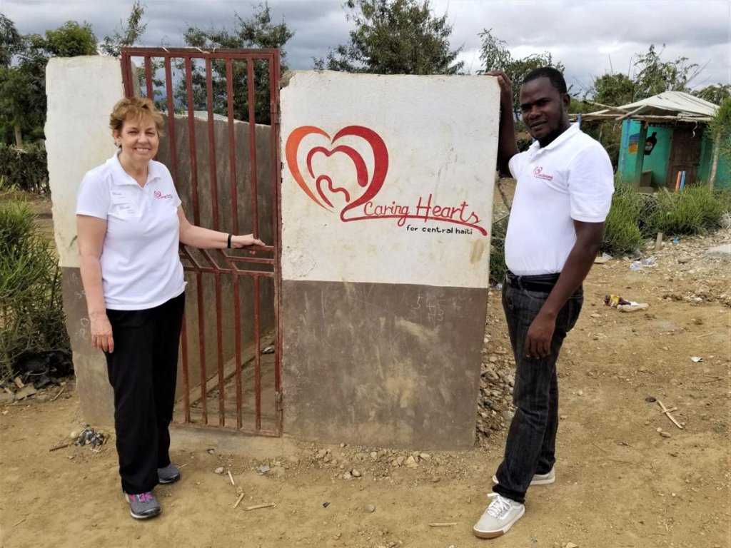 A man and a woman standing in front of a sign 'Caring Hearts for Central Haiti'