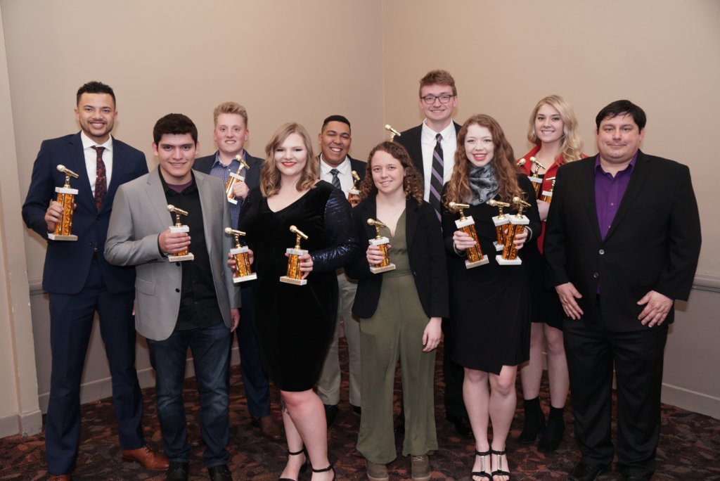 Group posing together for a photo and holding awards