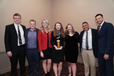 A group of people posing for a photo in a line with a woman at the center holding an award