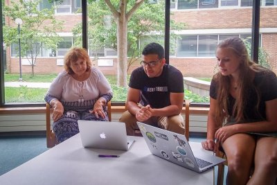 Three people sitting at a table looking at two laptops.