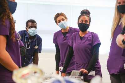 Three nursing students wearing purple scrubs and masks look off-camera